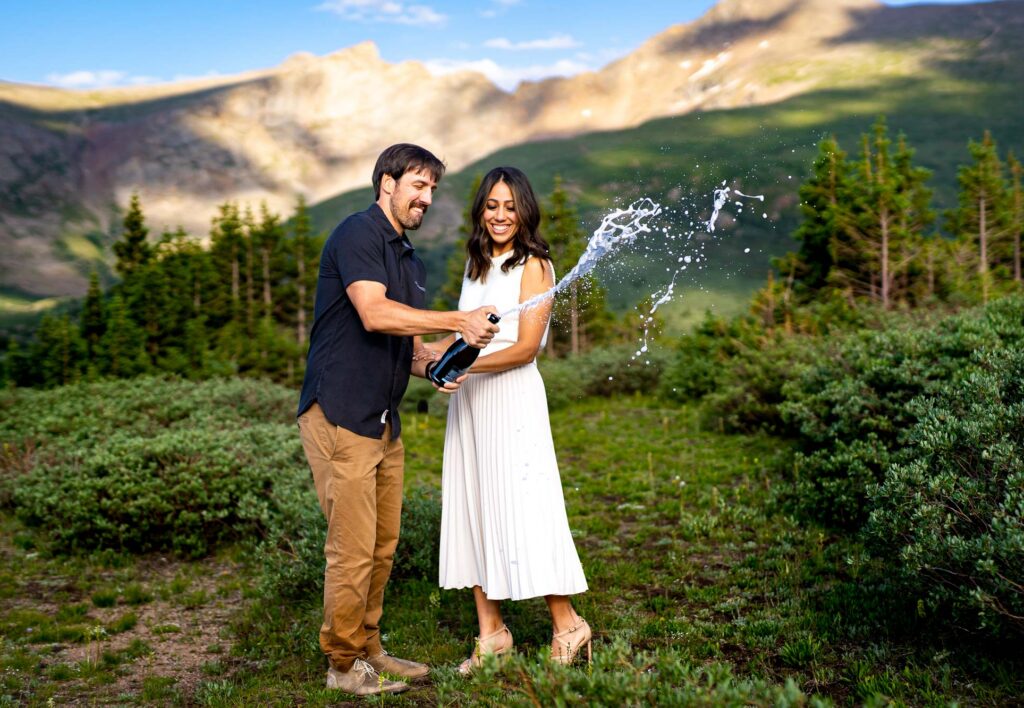 Bride and groom pop a bottle of champagne at the summit trailhead at Guanella Pass in Colorado during wildflower season.