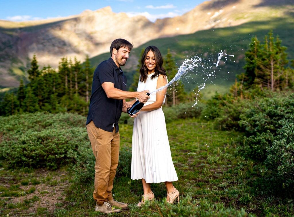 Bride and groom pop a bottle of champagne at the summit trailhead at Guanella Pass in Colorado during wildflower season.