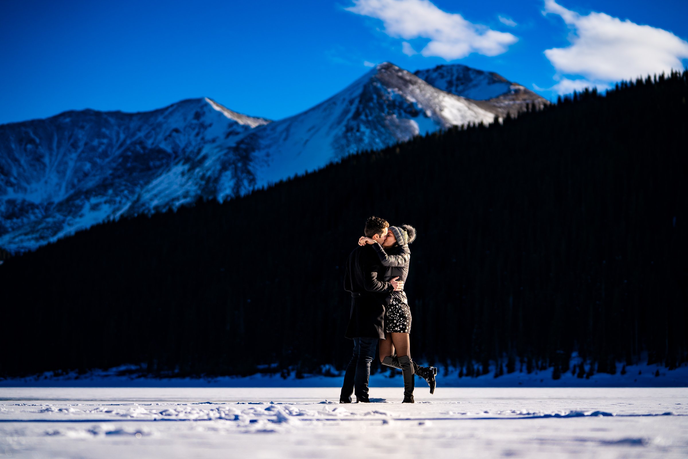 Engaged couple kisses while standing on a frozen lake with snowcapped mountains in the background, Engagement Session, Engagement Photos, Engagement Photos Inspiration, Engagement Photography, Engagement Photographer, Winter Engagement Photos, Proposal Photos, Proposal Photographer, Proposal Photography, Winter Proposal, Mountain Proposal, Proposal Inspiration, Summit County engagement session, Summit County engagement photos, Summit County engagement photography, Summit County engagement photographer, Summit County engagement inspiration, Colorado engagement session, Colorado engagement photos, Colorado engagement photography, Colorado engagement photographer, Colorado engagement inspiration, Clinton Gulch Engagement