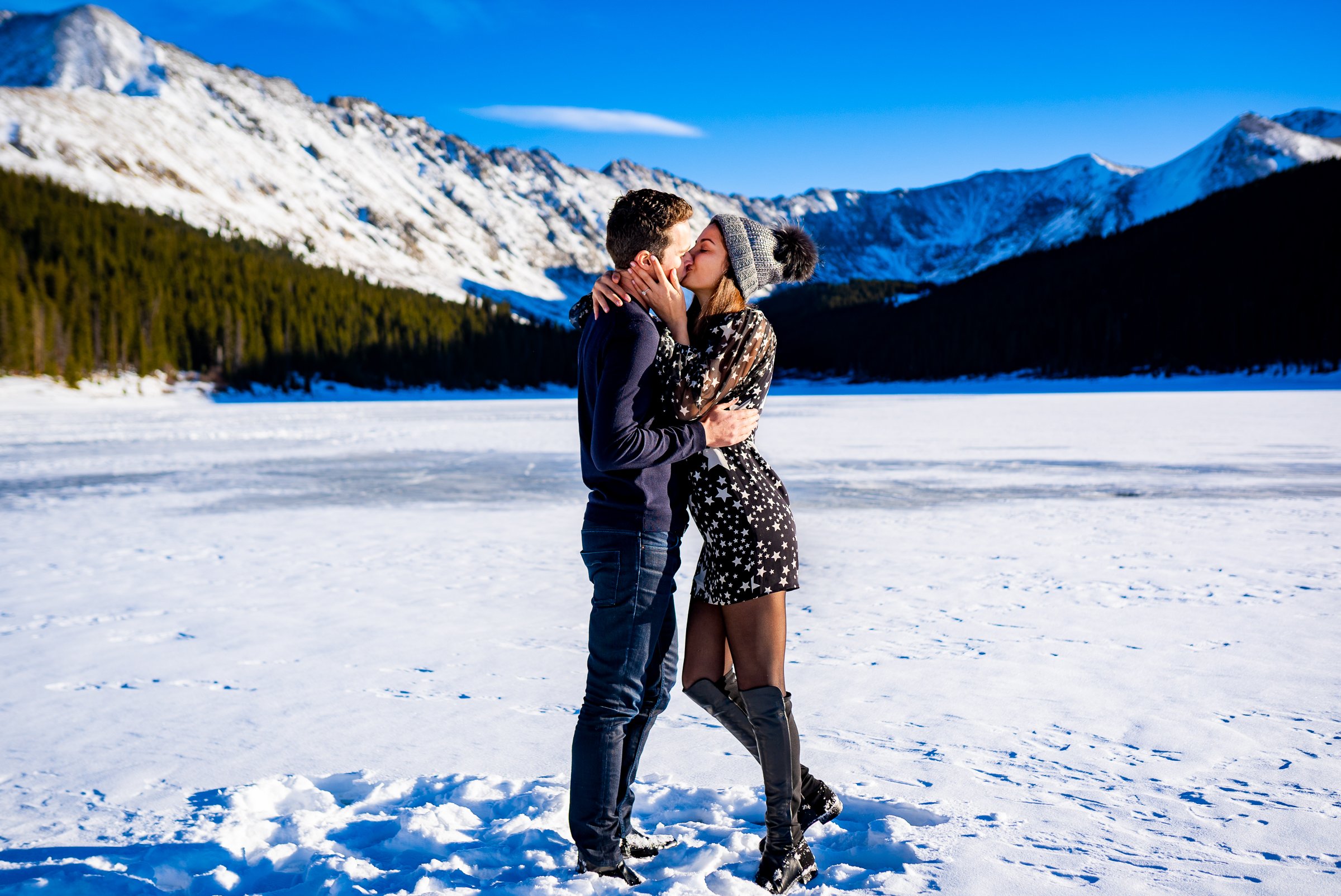 Newly engaged couple celebrate their proposal with a kiss on a frozen lake with snowcapped mountains in the background, Engagement Session, Engagement Photos, Engagement Photos Inspiration, Engagement Photography, Engagement Photographer, Winter Engagement Photos, Proposal Photos, Proposal Photographer, Proposal Photography, Winter Proposal, Mountain Proposal, Proposal Inspiration, Summit County engagement session, Summit County engagement photos, Summit County engagement photography, Summit County engagement photographer, Summit County engagement inspiration, Colorado engagement session, Colorado engagement photos, Colorado engagement photography, Colorado engagement photographer, Colorado engagement inspiration, Clinton Gulch Engagement