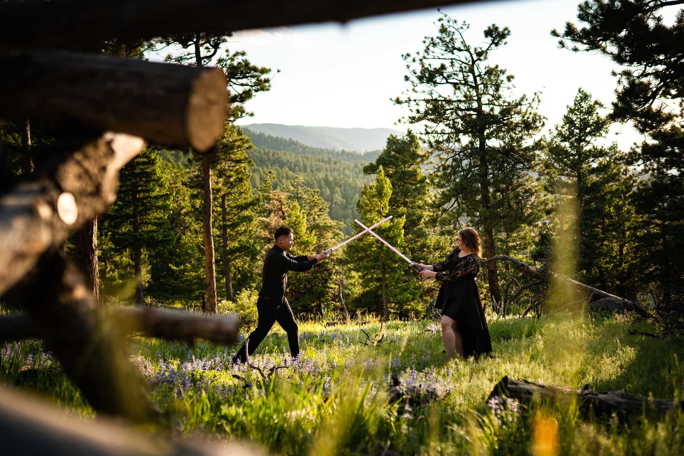 Engaged couple jumps into cosplay with their light sabers in the forest during golden hour, Engagement Session, Engagement Photos, Engagement Photos Inspiration, Engagement Photography, Engagement Photographer, Summer Engagement Photos, Mountain Engagement Photos, Lost Gulch Overlook engagement session, Lost Gulch Overlook engagement photos, Lost Gulch Overlook engagement photography, Lost Gulch Overlook engagement photographer, Lost Gulch Overlook  engagement inspiration, Boulder engagement session, Boulder engagement photos, Boulder engagement photography, Boulder engagement photographer, Boulder engagement inspiration, Colorado engagement session, Colorado engagement photos, Colorado engagement photography, Colorado engagement photographer, Colorado engagement inspiration