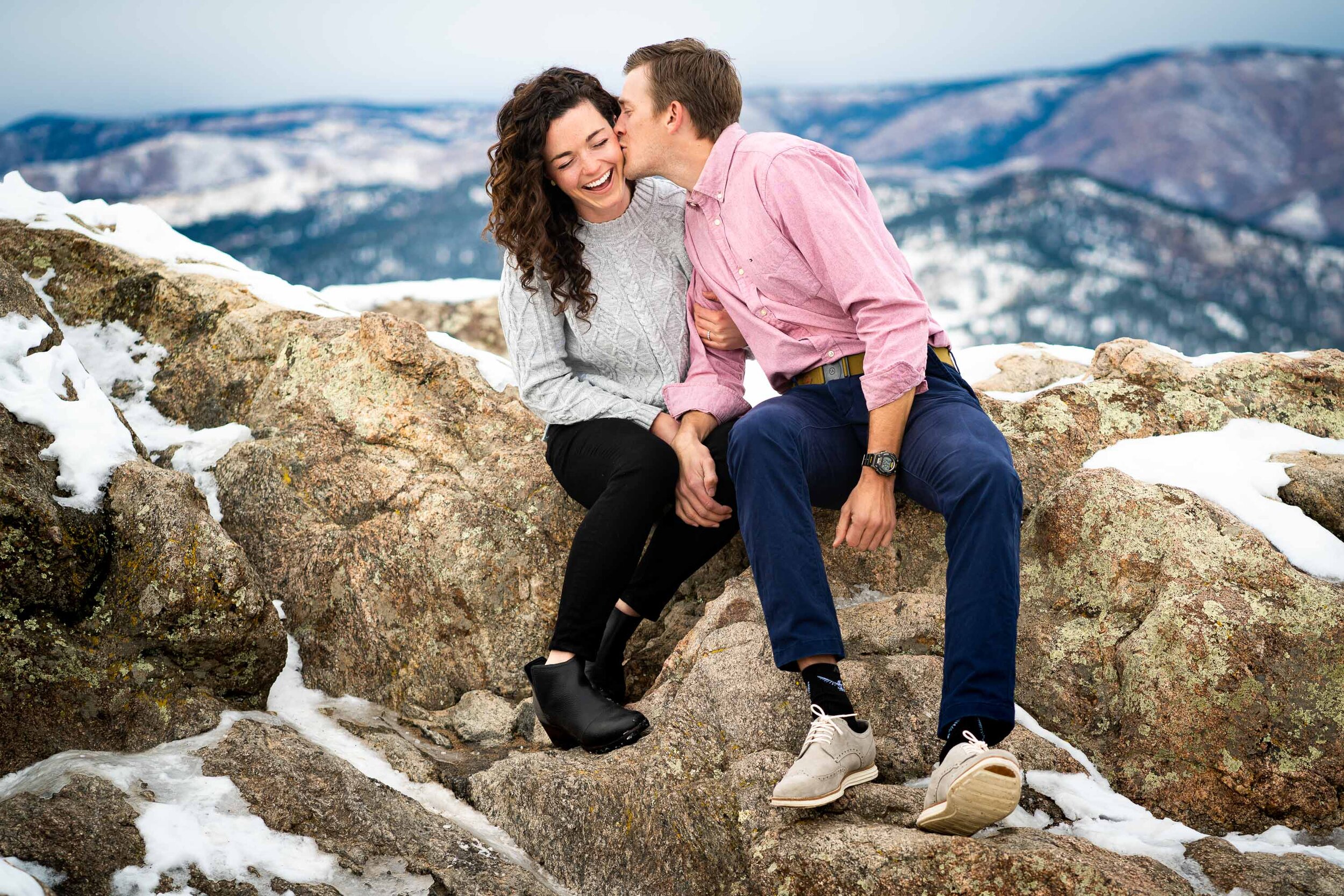 Engaged couple poses for portraits on a rocky ledge overlooking the snow-capped Rocky Mountains in the distance, Engagement Session, Engagement Photos, Engagement Photos Inspiration, Engagement Photography, Engagement Photographer, Winter Engagement Photos, Mountain Engagement Photos, Lost Gulch Overlook engagement session, Lost Gulch Overlook engagement photos, Lost Gulch Overlook engagement photography, Lost Gulch Overlook engagement photographer, Lost Gulch Overlook  engagement inspiration, Boulder engagement session, Boulder engagement photos, Boulder engagement photography, Boulder engagement photographer, Boulder engagement inspiration, Colorado engagement session, Colorado engagement photos, Colorado engagement photography, Colorado engagement photographer, Colorado engagement inspiration