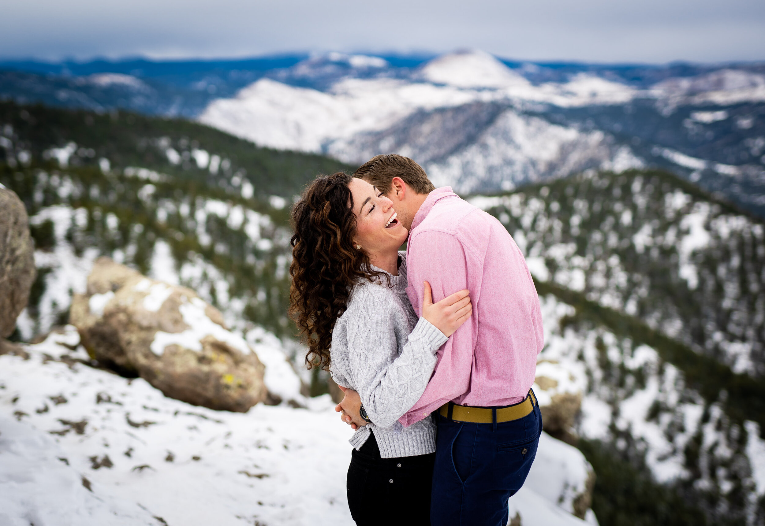 Engaged couple poses for portraits on a rocky ledge overlooking the snow-capped Rocky Mountains in the distance, Engagement Session, Engagement Photos, Engagement Photos Inspiration, Engagement Photography, Engagement Photographer, Winter Engagement Photos, Mountain Engagement Photos, Lost Gulch Overlook engagement session, Lost Gulch Overlook engagement photos, Lost Gulch Overlook engagement photography, Lost Gulch Overlook engagement photographer, Lost Gulch Overlook  engagement inspiration, Boulder engagement session, Boulder engagement photos, Boulder engagement photography, Boulder engagement photographer, Boulder engagement inspiration, Colorado engagement session, Colorado engagement photos, Colorado engagement photography, Colorado engagement photographer, Colorado engagement inspiration