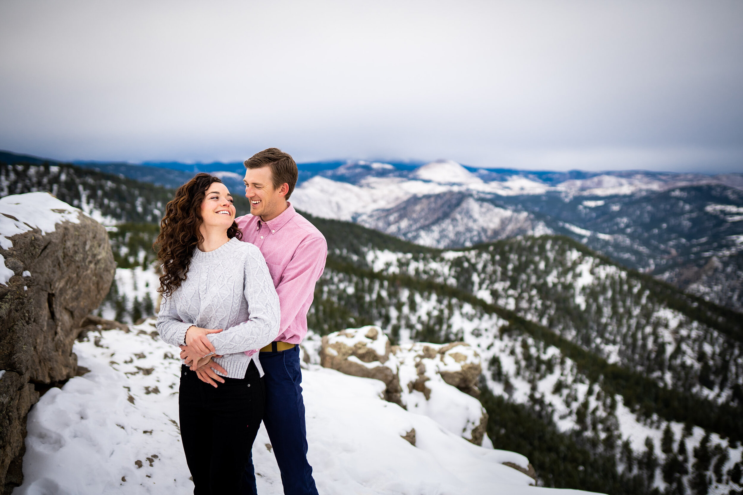 Engaged couple poses for portraits on a rocky ledge overlooking the snow-capped Rocky Mountains in the distance, Engagement Session, Engagement Photos, Engagement Photos Inspiration, Engagement Photography, Engagement Photographer, Winter Engagement Photos, Mountain Engagement Photos, Lost Gulch Overlook engagement session, Lost Gulch Overlook engagement photos, Lost Gulch Overlook engagement photography, Lost Gulch Overlook engagement photographer, Lost Gulch Overlook  engagement inspiration, Boulder engagement session, Boulder engagement photos, Boulder engagement photography, Boulder engagement photographer, Boulder engagement inspiration, Colorado engagement session, Colorado engagement photos, Colorado engagement photography, Colorado engagement photographer, Colorado engagement inspiration