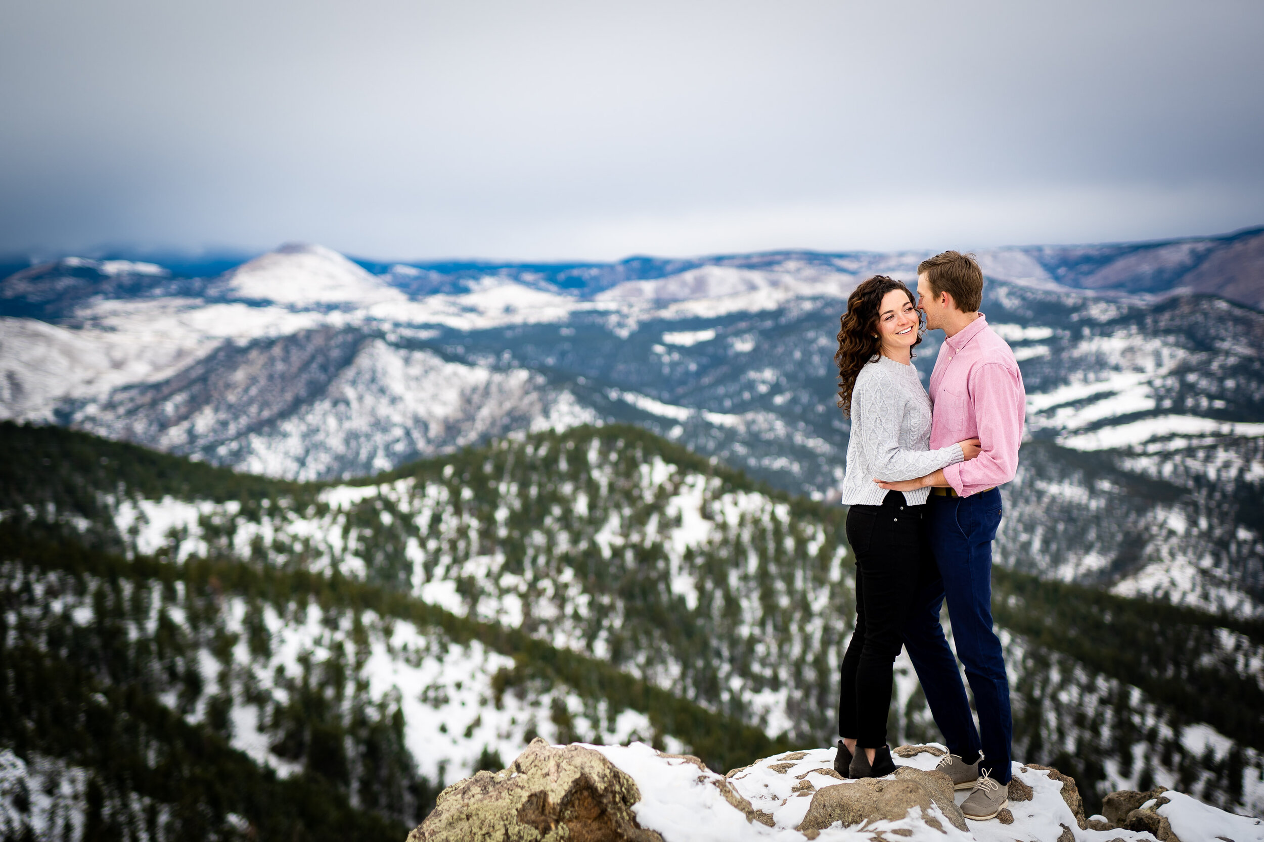 Engaged couple poses for portraits on a rocky ledge overlooking the snow-capped Rocky Mountains in the distance, Engagement Session, Engagement Photos, Engagement Photos Inspiration, Engagement Photography, Engagement Photographer, Winter Engagement Photos, Mountain Engagement Photos, Lost Gulch Overlook engagement session, Lost Gulch Overlook engagement photos, Lost Gulch Overlook engagement photography, Lost Gulch Overlook engagement photographer, Lost Gulch Overlook  engagement inspiration, Boulder engagement session, Boulder engagement photos, Boulder engagement photography, Boulder engagement photographer, Boulder engagement inspiration, Colorado engagement session, Colorado engagement photos, Colorado engagement photography, Colorado engagement photographer, Colorado engagement inspiration