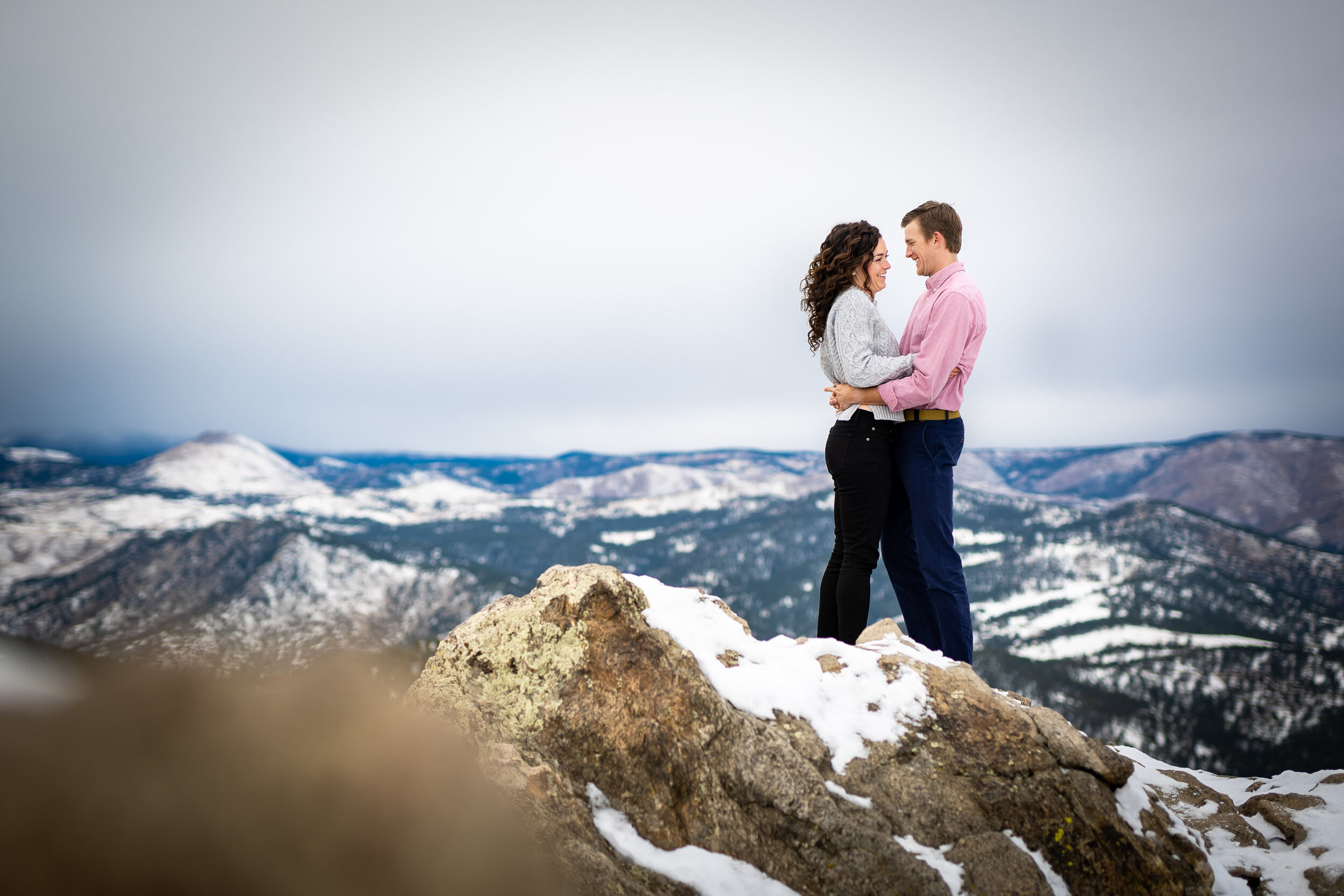 Engaged couple poses for portraits on a rocky ledge overlooking the snow-capped Rocky Mountains in the distance, Engagement Session, Engagement Photos, Engagement Photos Inspiration, Engagement Photography, Engagement Photographer, Winter Engagement Photos, Mountain Engagement Photos, Lost Gulch Overlook engagement session, Lost Gulch Overlook engagement photos, Lost Gulch Overlook engagement photography, Lost Gulch Overlook engagement photographer, Lost Gulch Overlook  engagement inspiration, Boulder engagement session, Boulder engagement photos, Boulder engagement photography, Boulder engagement photographer, Boulder engagement inspiration, Colorado engagement session, Colorado engagement photos, Colorado engagement photography, Colorado engagement photographer, Colorado engagement inspiration