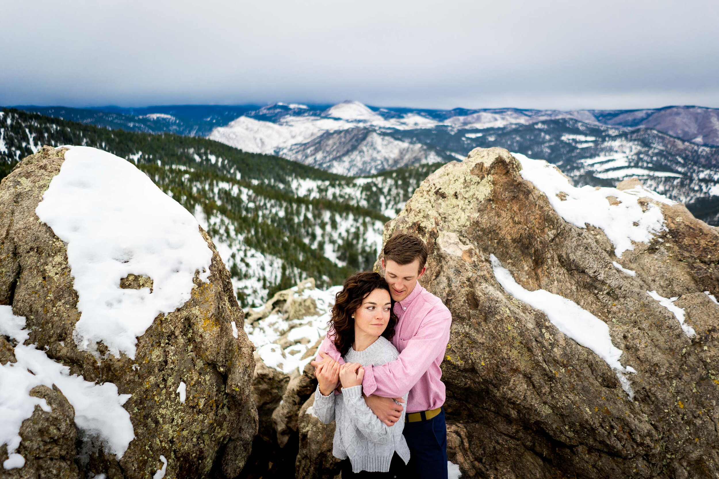 Engaged couple poses for portraits on a rocky ledge overlooking the snow-capped Rocky Mountains in the distance, Engagement Session, Engagement Photos, Engagement Photos Inspiration, Engagement Photography, Engagement Photographer, Winter Engagement Photos, Mountain Engagement Photos, Lost Gulch Overlook engagement session, Lost Gulch Overlook engagement photos, Lost Gulch Overlook engagement photography, Lost Gulch Overlook engagement photographer, Lost Gulch Overlook  engagement inspiration, Boulder engagement session, Boulder engagement photos, Boulder engagement photography, Boulder engagement photographer, Boulder engagement inspiration, Colorado engagement session, Colorado engagement photos, Colorado engagement photography, Colorado engagement photographer, Colorado engagement inspiration