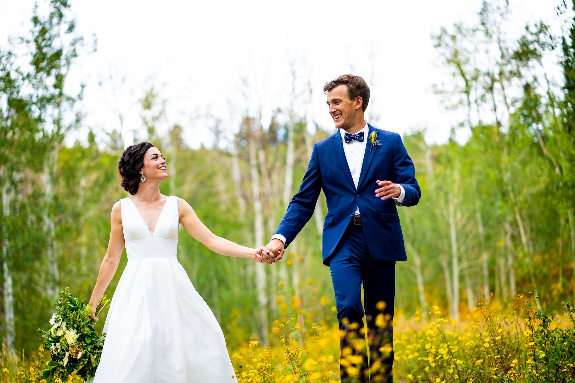 Bride and groom walk while holding hands in a field of wildflowers surrounded by aspens in a meadow, wedding, wedding photos, wedding photography, wedding photographer, wedding inspiration, wedding photo inspiration, wedding portraits, wedding ceremony, wedding reception, mountain wedding, Catholic Church wedding, Catholic Church wedding photos, Catholic Church wedding photography, Catholic Church wedding photographer, Catholic Church wedding inspiration, Catholic Church wedding venue, Steamboat Springs wedding, Steamboat Springs wedding photos, Steamboat Springs wedding photography, Steamboat Springs wedding photographer, Colorado wedding, Colorado wedding photos, Colorado wedding photography, Colorado wedding photographer, Colorado mountain wedding, Colorado wedding inspiration