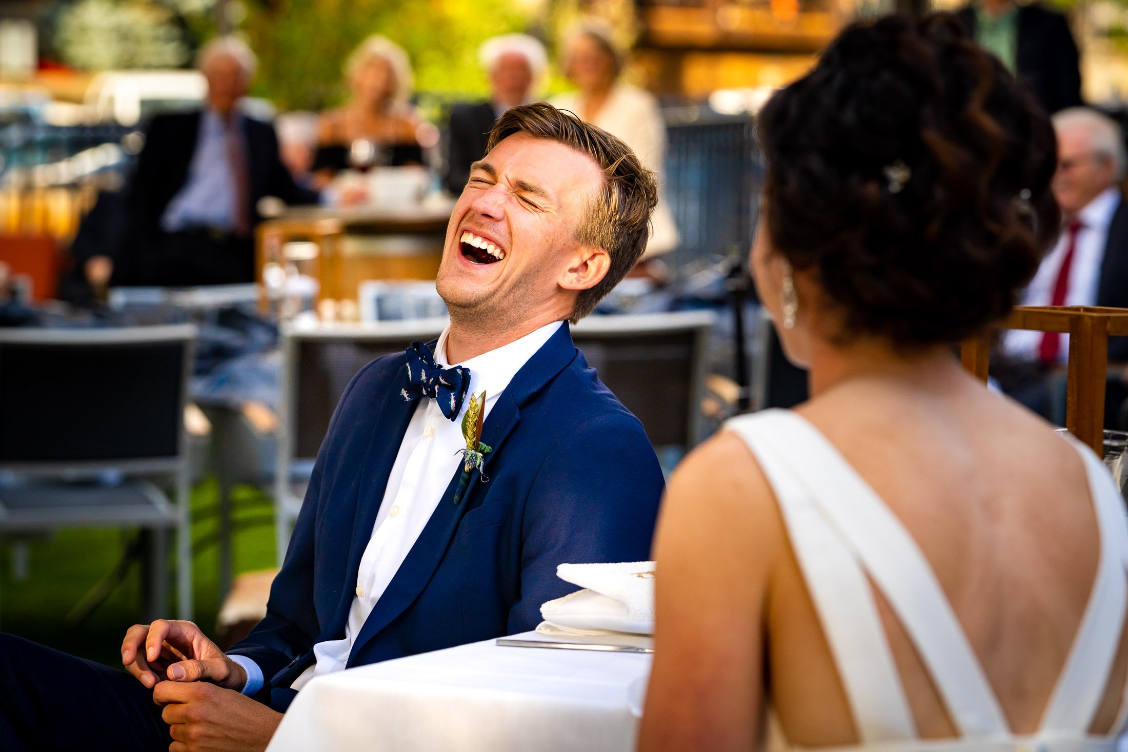 Bride and groom react to reception speeches while sitting on outdoor patio during the wedding reception, wedding, wedding photos, wedding photography, wedding photographer, wedding inspiration, wedding photo inspiration, wedding portraits, wedding ceremony, wedding reception, mountain wedding, Catholic Church wedding, Catholic Church wedding photos, Catholic Church wedding photography, Catholic Church wedding photographer, Catholic Church wedding inspiration, Catholic Church wedding venue, Steamboat Springs wedding, Steamboat Springs wedding photos, Steamboat Springs wedding photography, Steamboat Springs wedding photographer, Colorado wedding, Colorado wedding photos, Colorado wedding photography, Colorado wedding photographer, Colorado mountain wedding, Colorado wedding inspiration