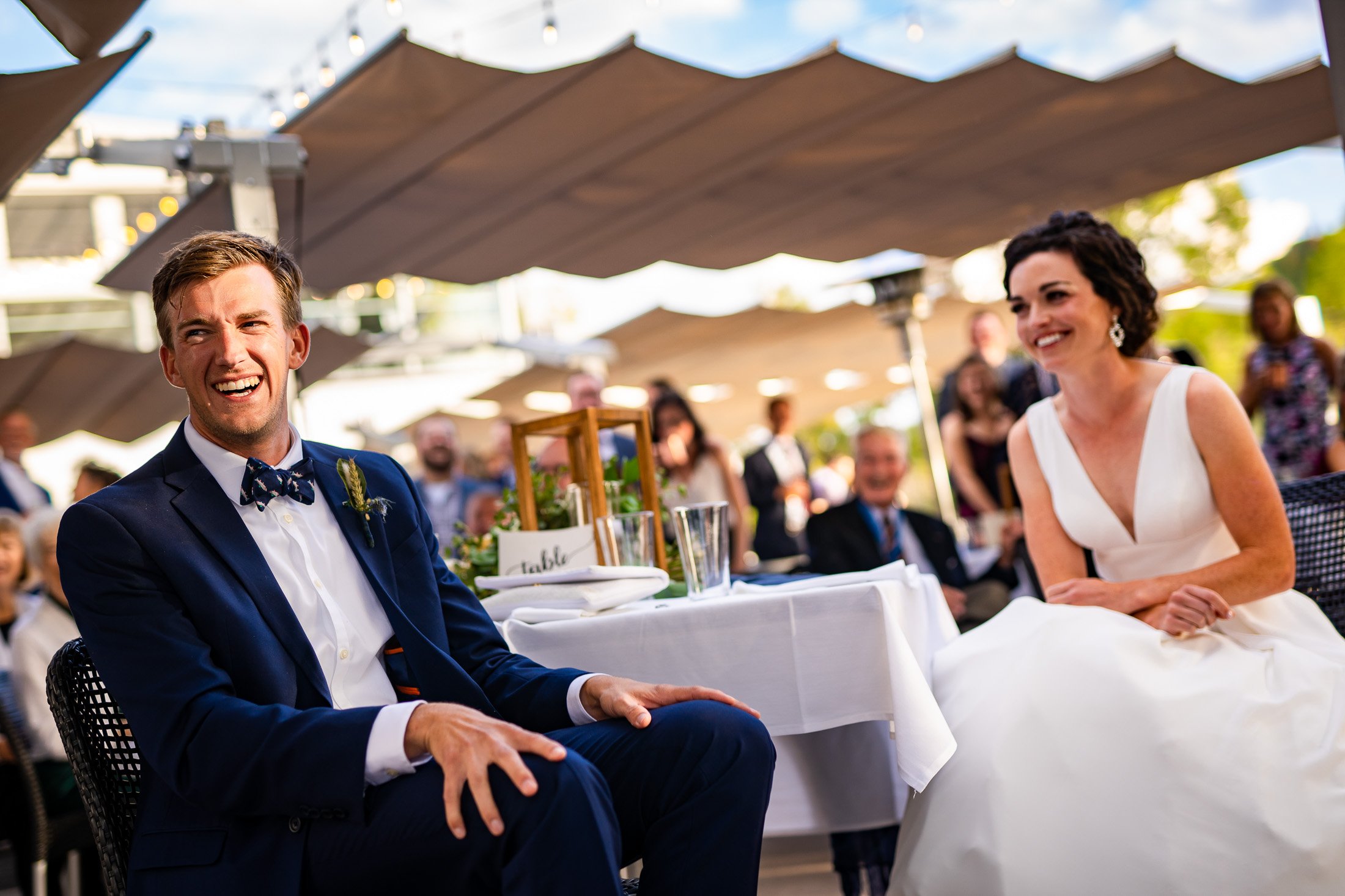 Bride and groom react to reception speeches while sitting on outdoor patio during the wedding reception, wedding, wedding photos, wedding photography, wedding photographer, wedding inspiration, wedding photo inspiration, wedding portraits, wedding ceremony, wedding reception, mountain wedding, Catholic Church wedding, Catholic Church wedding photos, Catholic Church wedding photography, Catholic Church wedding photographer, Catholic Church wedding inspiration, Catholic Church wedding venue, Steamboat Springs wedding, Steamboat Springs wedding photos, Steamboat Springs wedding photography, Steamboat Springs wedding photographer, Colorado wedding, Colorado wedding photos, Colorado wedding photography, Colorado wedding photographer, Colorado mountain wedding, Colorado wedding inspiration