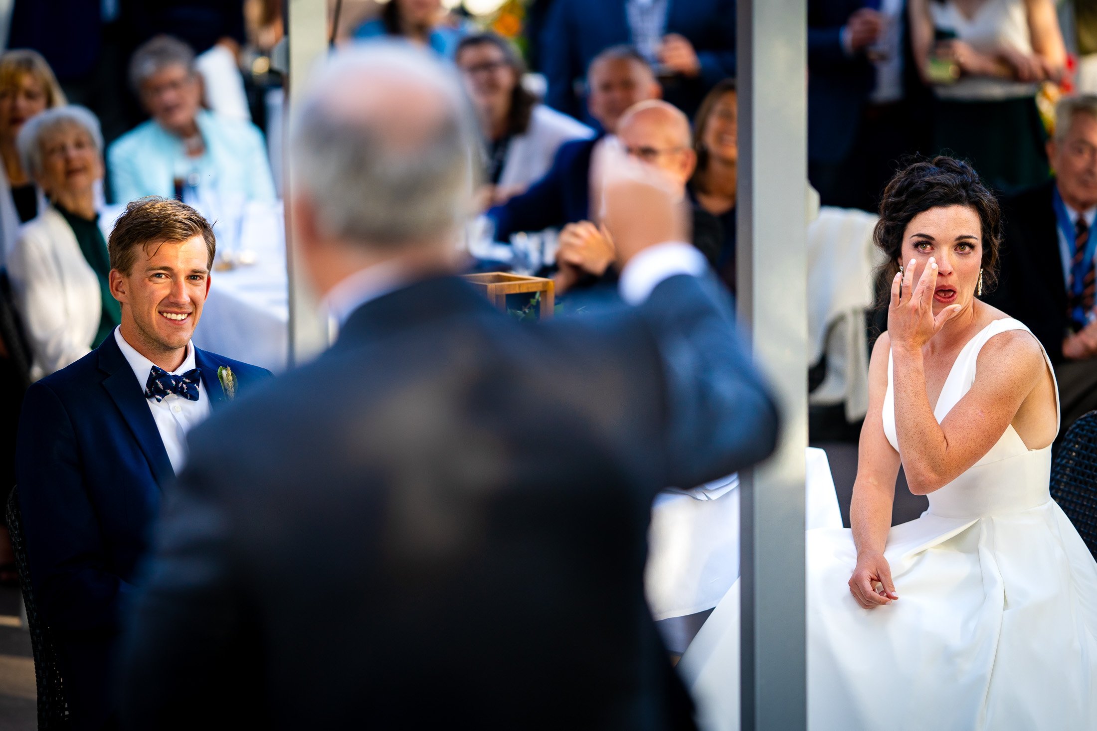 Bride and groom react to reception speeches while sitting on outdoor patio during the wedding reception, wedding, wedding photos, wedding photography, wedding photographer, wedding inspiration, wedding photo inspiration, wedding portraits, wedding ceremony, wedding reception, mountain wedding, Catholic Church wedding, Catholic Church wedding photos, Catholic Church wedding photography, Catholic Church wedding photographer, Catholic Church wedding inspiration, Catholic Church wedding venue, Steamboat Springs wedding, Steamboat Springs wedding photos, Steamboat Springs wedding photography, Steamboat Springs wedding photographer, Colorado wedding, Colorado wedding photos, Colorado wedding photography, Colorado wedding photographer, Colorado mountain wedding, Colorado wedding inspiration