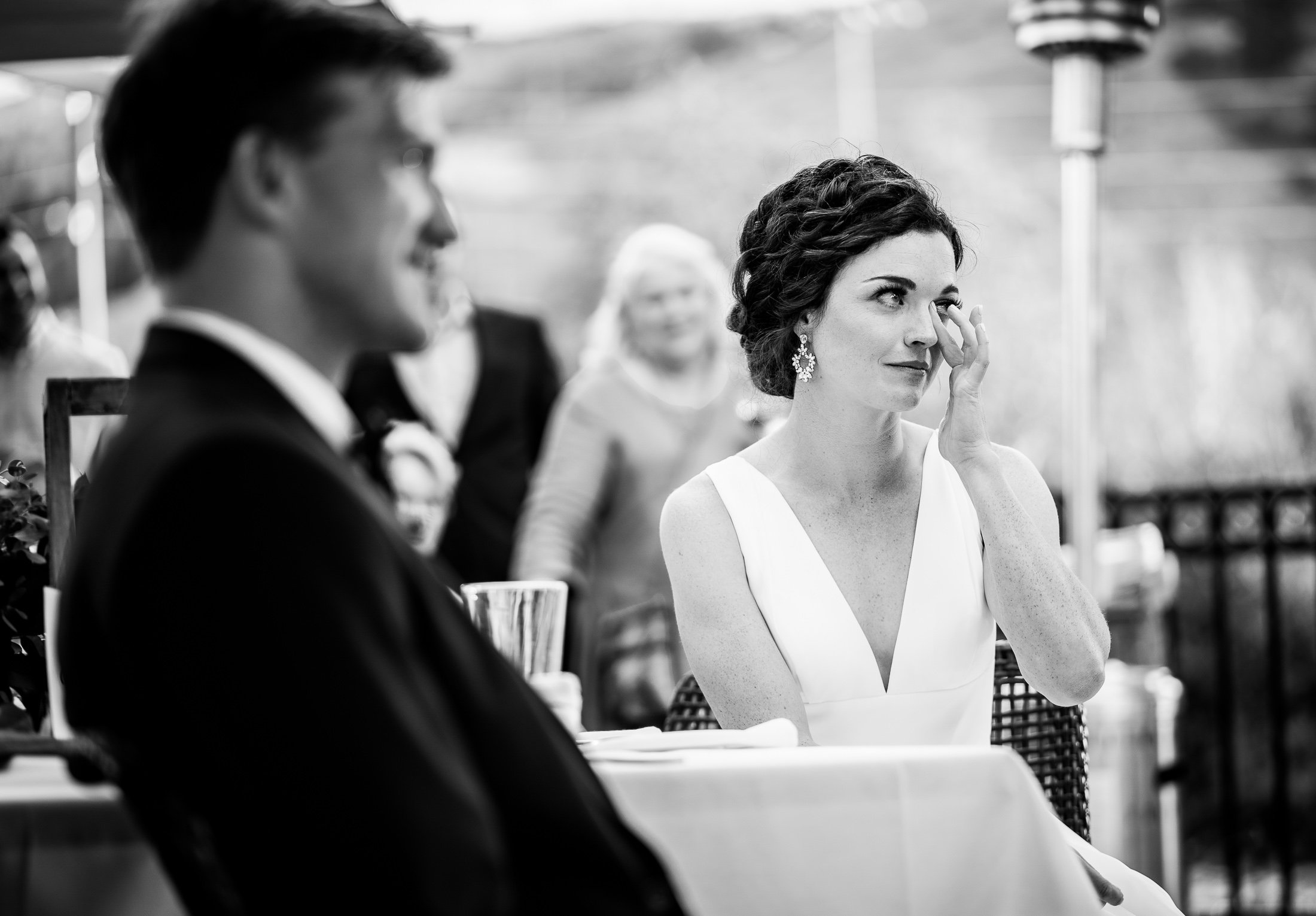 Bride and groom react to reception speeches while sitting on outdoor patio during the wedding reception, wedding, wedding photos, wedding photography, wedding photographer, wedding inspiration, wedding photo inspiration, wedding portraits, wedding ceremony, wedding reception, mountain wedding, Catholic Church wedding, Catholic Church wedding photos, Catholic Church wedding photography, Catholic Church wedding photographer, Catholic Church wedding inspiration, Catholic Church wedding venue, Steamboat Springs wedding, Steamboat Springs wedding photos, Steamboat Springs wedding photography, Steamboat Springs wedding photographer, Colorado wedding, Colorado wedding photos, Colorado wedding photography, Colorado wedding photographer, Colorado mountain wedding, Colorado wedding inspiration