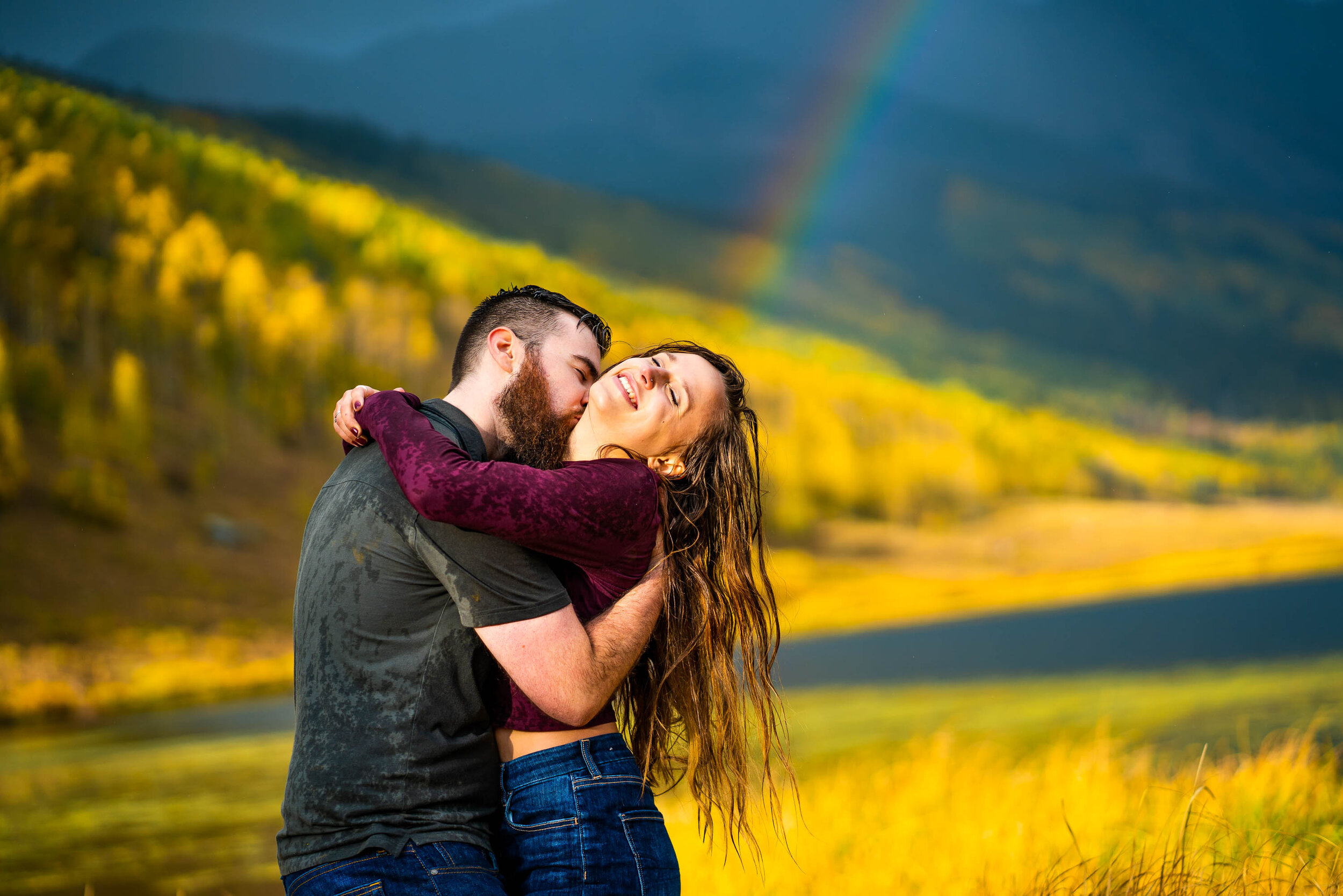 Engaged couple embraces for a portrait during a rainstorm with a double rainbow behind them arching over Piney Lake, Engagement Session, Engagement Photos, Engagement Photos Inspiration, Engagement Photography, Engagement Photographer, Fall Engagement Photos, Mountain Engagement Photos, Piney River Ranch engagement photos, Vail engagement session, Vail engagement photos, Vail engagement photography, Vail engagement photographer, Vail engagement inspiration, Colorado engagement session, Colorado engagement photos, Colorado engagement photography, Colorado engagement photographer, Colorado engagement inspiration