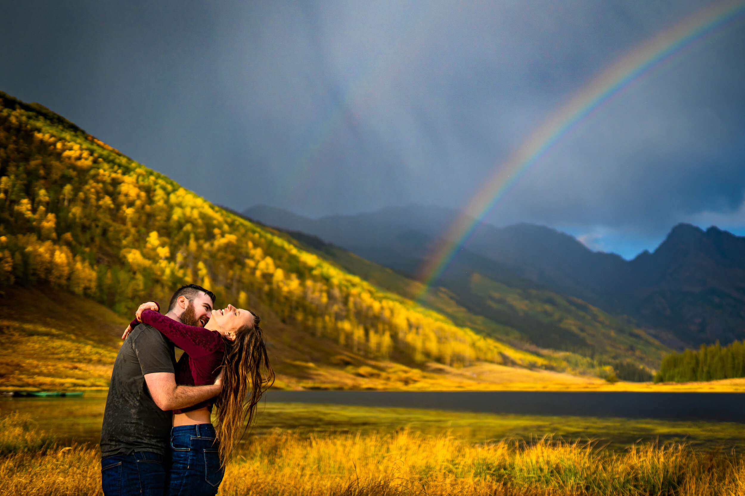 Engaged couple embraces for a portrait during a rainstorm with a double rainbow behind them arching over Piney Lake, Engagement Session, Engagement Photos, Engagement Photos Inspiration, Engagement Photography, Engagement Photographer, Fall Engagement Photos, Mountain Engagement Photos, Piney River Ranch engagement photos, Vail engagement session, Vail engagement photos, Vail engagement photography, Vail engagement photographer, Vail engagement inspiration, Colorado engagement session, Colorado engagement photos, Colorado engagement photography, Colorado engagement photographer, Colorado engagement inspiration