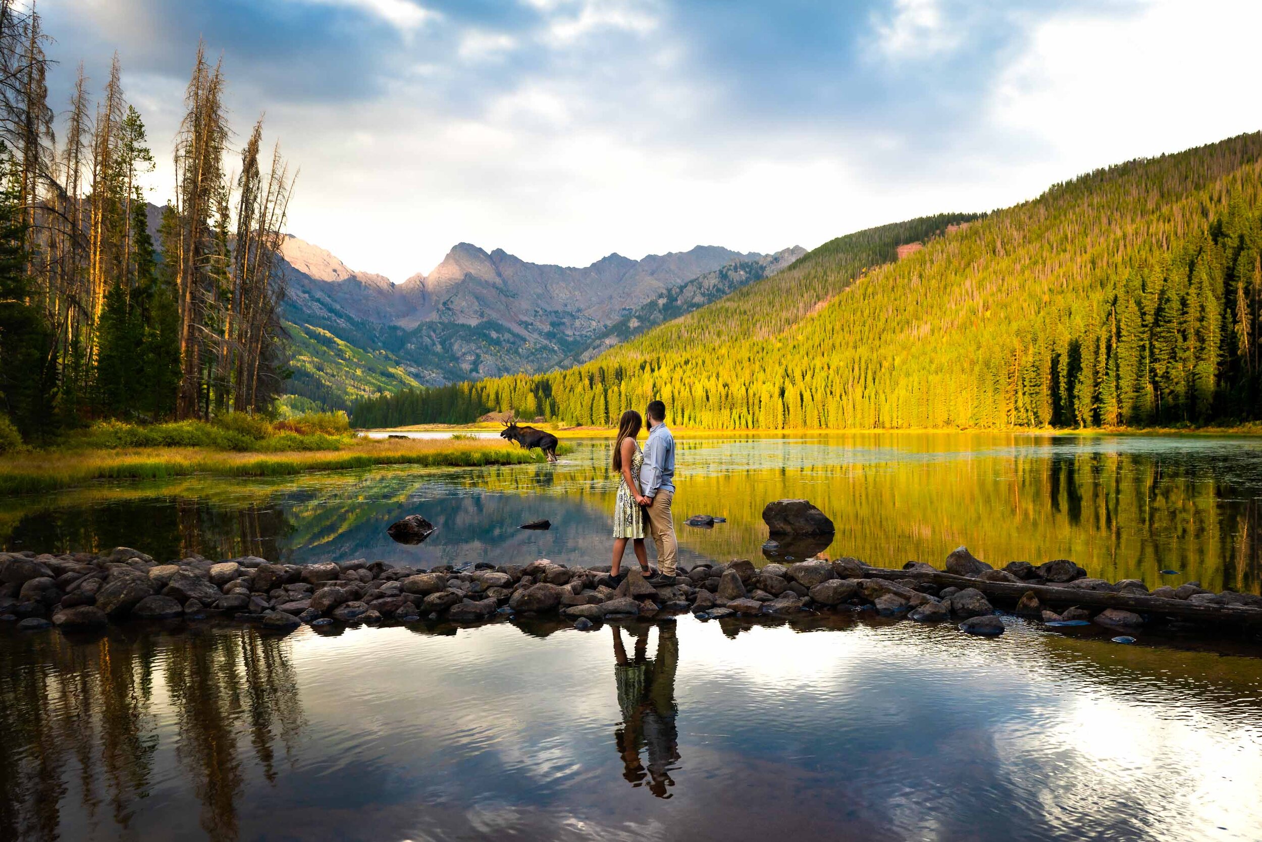 Engaged couple embraces as they watch a moose walk by during a portrait session by the lake during golden hour in the peak of the fall season with foliage all around, Engagement Session, Engagement Photos, Engagement Photos Inspiration, Engagement Photography, Engagement Photographer, Fall Engagement Photos, Mountain Engagement Photos, Piney River Ranch engagement photos, Vail engagement session, Vail engagement photos, Vail engagement photography, Vail engagement photographer, Vail engagement inspiration, Colorado engagement session, Colorado engagement photos, Colorado engagement photography, Colorado engagement photographer, Colorado engagement inspiration