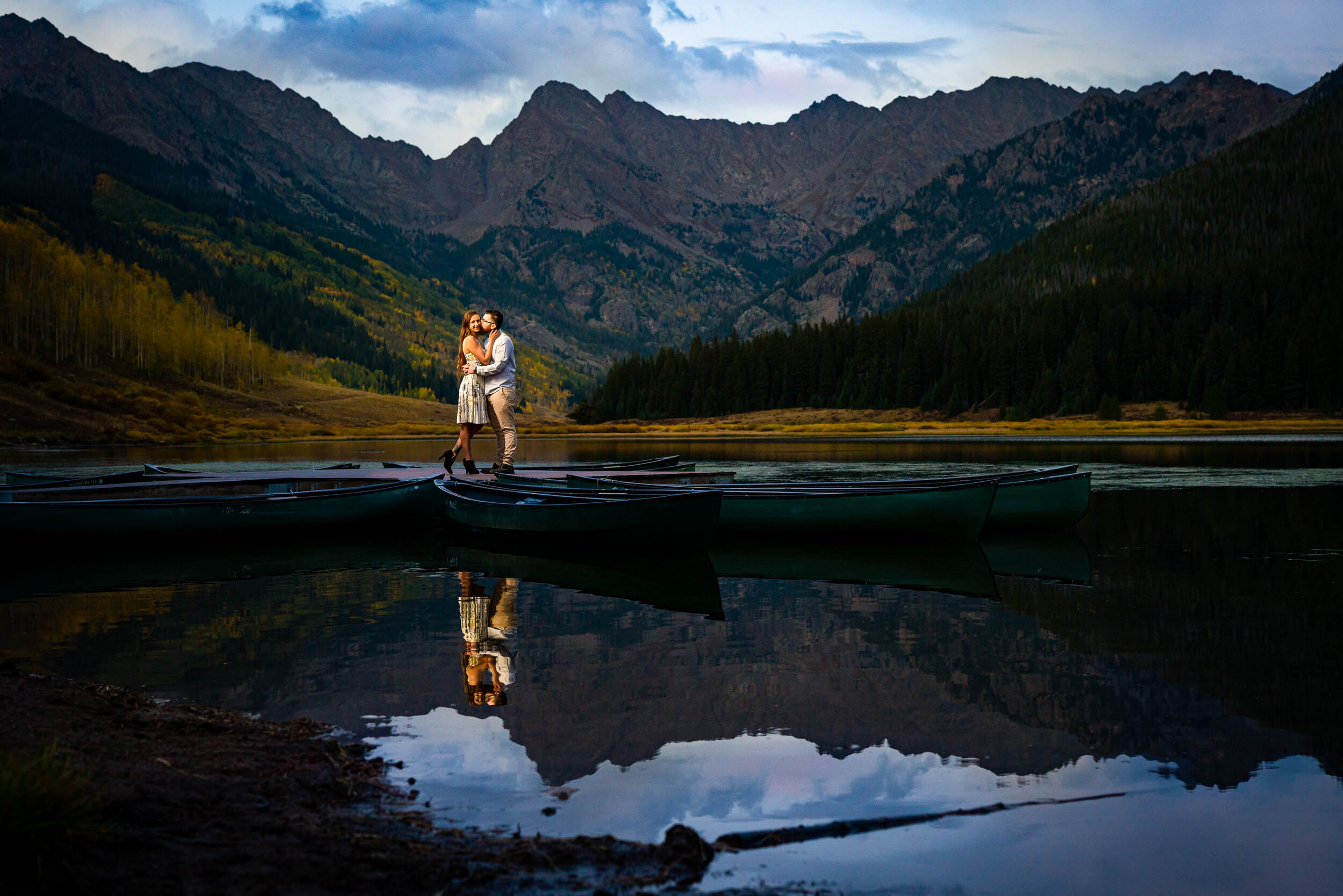 Engaged couple shares a kiss on the dock at blue hour surrounded by water with the mountains in the background, Engagement Session, Engagement Photos, Engagement Photos Inspiration, Engagement Photography, Engagement Photographer, Fall Engagement Photos, Mountain Engagement Photos, Piney River Ranch engagement photos, Vail engagement session, Vail engagement photos, Vail engagement photography, Vail engagement photographer, Vail engagement inspiration, Colorado engagement session, Colorado engagement photos, Colorado engagement photography, Colorado engagement photographer, Colorado engagement inspiration