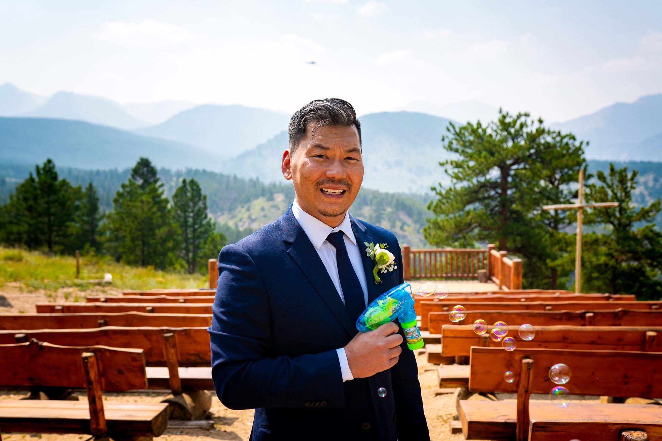 Groom holds a bubble gun in front of the ceremony site overlooking Rocky Mountain National Park in Colorado.