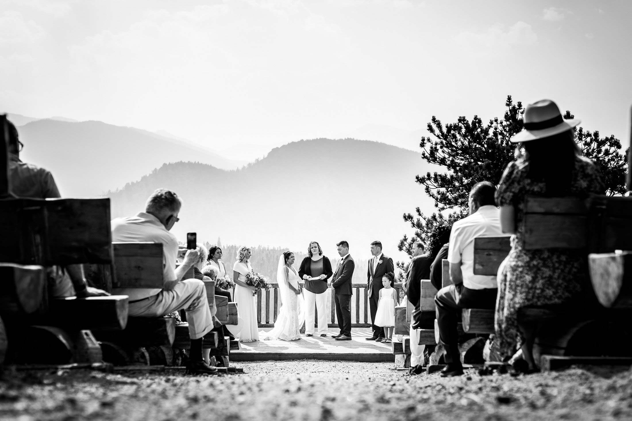 Bride and groom attend their ceremony as they stand alongside their wedding party on a wedding deck with the mountains in the background captured in black and white, wedding photos, wedding photography, wedding photographer, wedding inspiration, wedding photo inspiration, mountain wedding, YMCA of the Rockies wedding, YMCA of the Rockies wedding photos, YMCA of the Rockies wedding photography, YMCA of the Rockies wedding photographer, YMCA of the Rockies wedding inspiration, YMCA of the Rockies wedding venue, Estes Park wedding, Estes Park wedding photos, Estes Park wedding photography, Estes Park wedding photographer, Colorado wedding, Colorado wedding photos, Colorado wedding photography, Colorado wedding photographer, Colorado mountain wedding, Colorado wedding inspiration