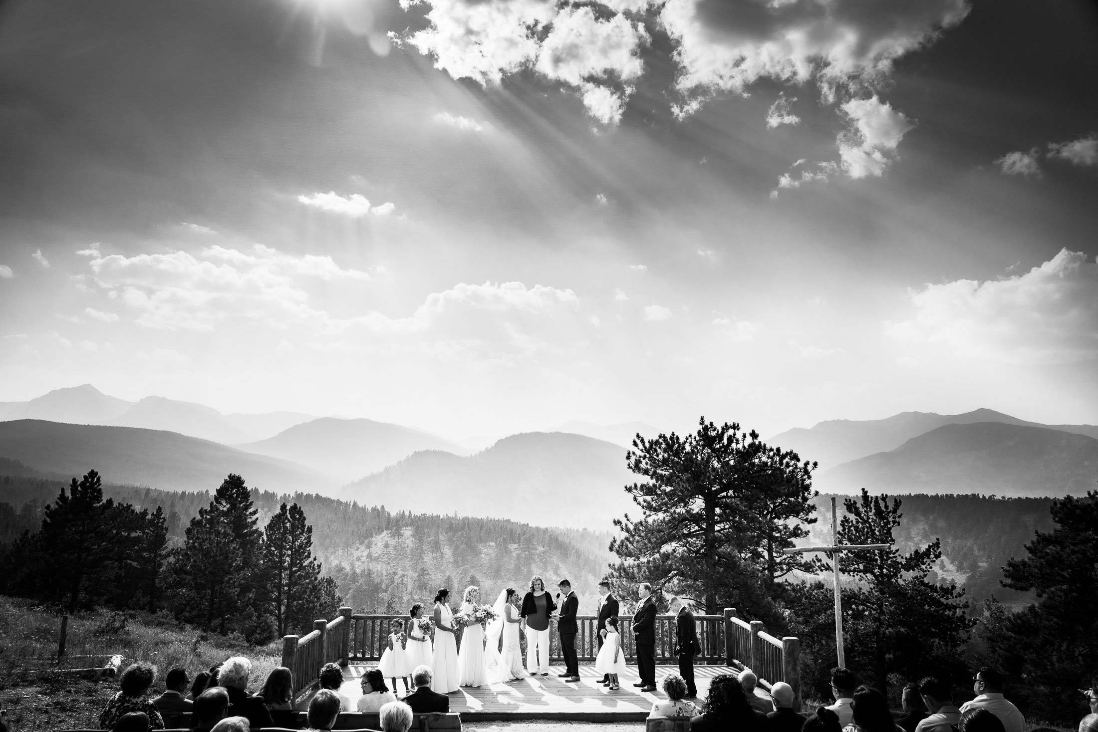 Bride and groom attend their ceremony as they stand alongside their wedding party on a wedding deck with the mountains in the background captured in black and white, wedding photos, wedding photography, wedding photographer, wedding inspiration, wedding photo inspiration, mountain wedding, YMCA of the Rockies wedding, YMCA of the Rockies wedding photos, YMCA of the Rockies wedding photography, YMCA of the Rockies wedding photographer, YMCA of the Rockies wedding inspiration, YMCA of the Rockies wedding venue, Estes Park wedding, Estes Park wedding photos, Estes Park wedding photography, Estes Park wedding photographer, Colorado wedding, Colorado wedding photos, Colorado wedding photography, Colorado wedding photographer, Colorado mountain wedding, Colorado wedding inspiration