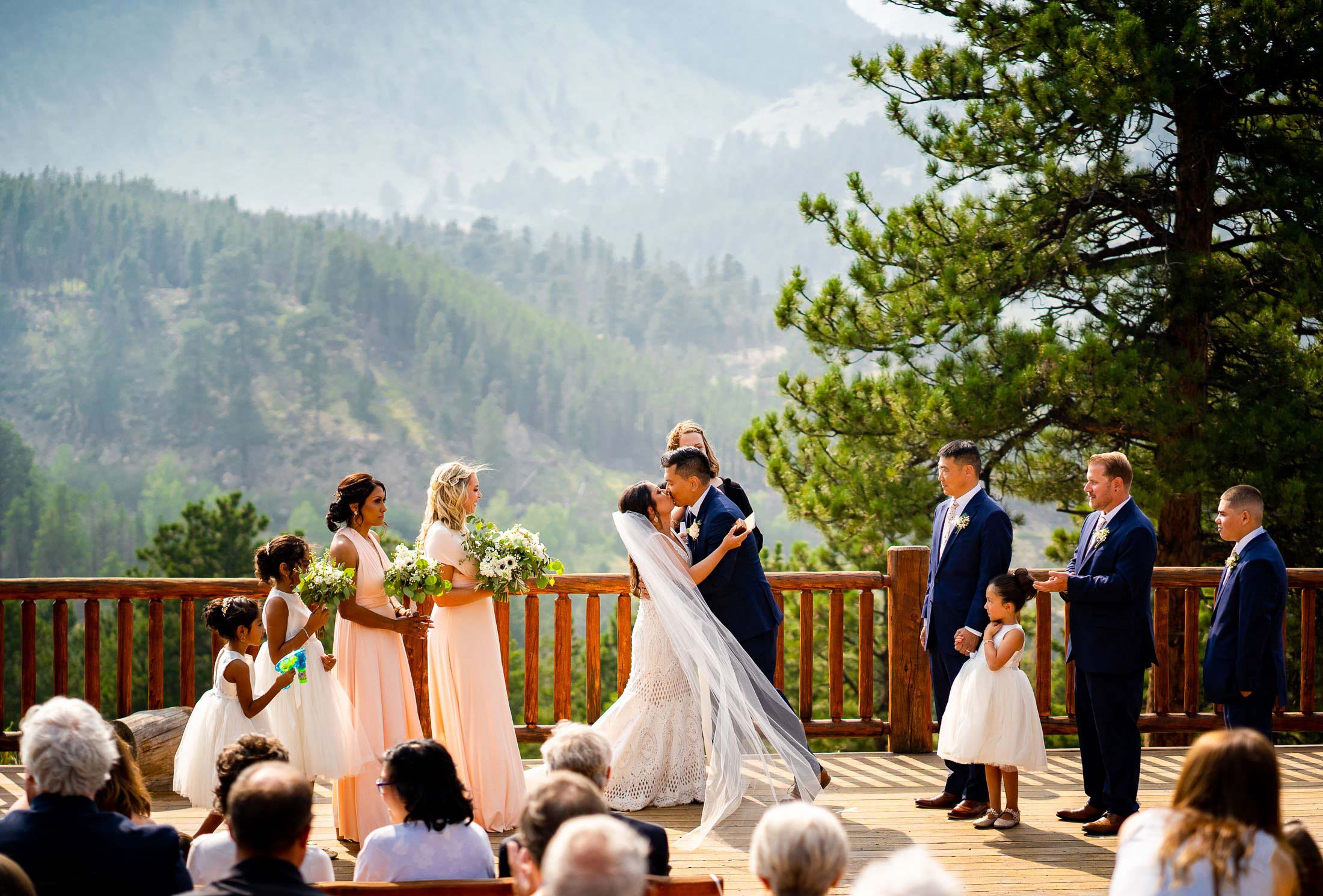Bride and groom share their first kiss during their wedding ceremony in the mountains as their wedding party cheers and celebrates, wedding photos, wedding photography, wedding photographer, wedding inspiration, wedding photo inspiration, mountain wedding, YMCA of the Rockies wedding, YMCA of the Rockies wedding photos, YMCA of the Rockies wedding photography, YMCA of the Rockies wedding photographer, YMCA of the Rockies wedding inspiration, YMCA of the Rockies wedding venue, Estes Park wedding, Estes Park wedding photos, Estes Park wedding photography, Estes Park wedding photographer, Colorado wedding, Colorado wedding photos, Colorado wedding photography, Colorado wedding photographer, Colorado mountain wedding, Colorado wedding inspiration