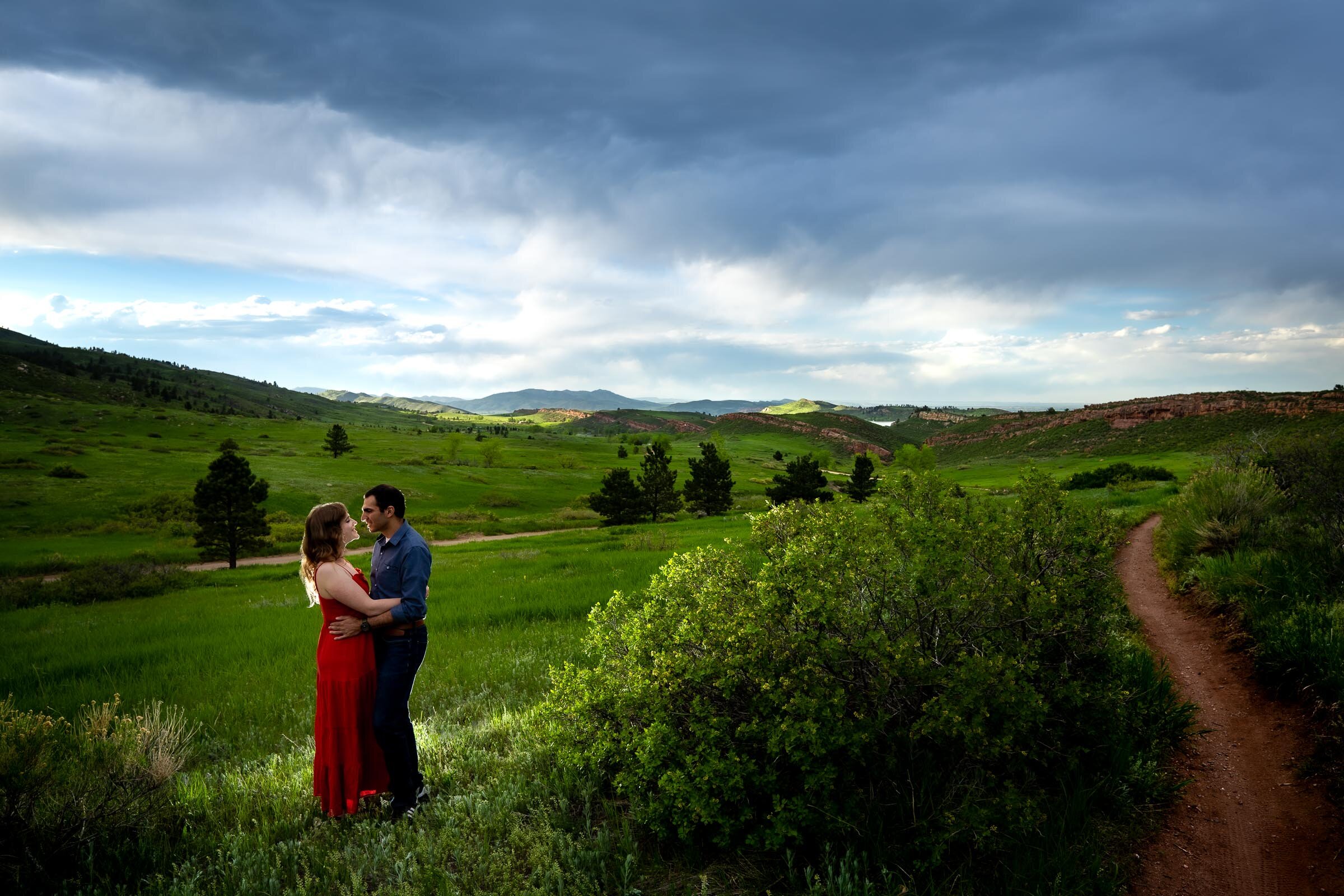 Engaged couple embraces in a luscious green landscape of rolling foothills during golden hour, Engagement Photos, Engagement Photo Inspiration, Engagement Photography, Engagement Photographer, Spring Engagement Photos, Fort Collins Engagement Photos, Fort Collins engagement photos, Fort Collins engagement photography, Fort Collins engagement photographer, Colorado engagement photos, Colorado engagement photography, Colorado engagement inspiration