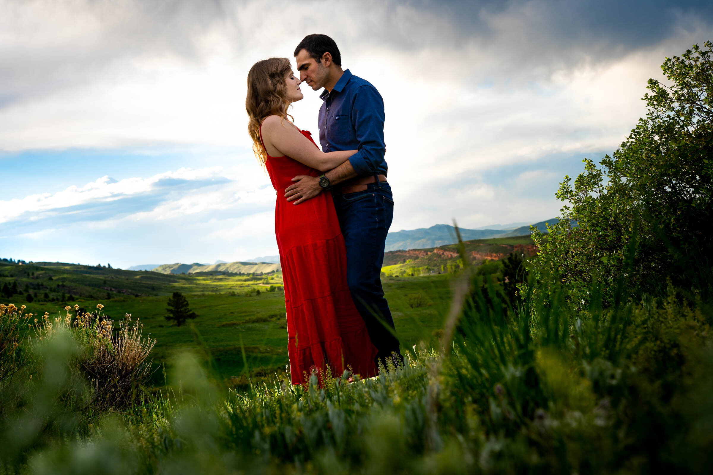 Engaged couple embraces in a luscious green landscape of rolling foothills during golden hour, Engagement Photos, Engagement Photo Inspiration, Engagement Photography, Engagement Photographer, Spring Engagement Photos, Fort Collins Engagement Photos, Fort Collins engagement photos, Fort Collins engagement photography, Fort Collins engagement photographer, Colorado engagement photos, Colorado engagement photography, Colorado engagement inspiration