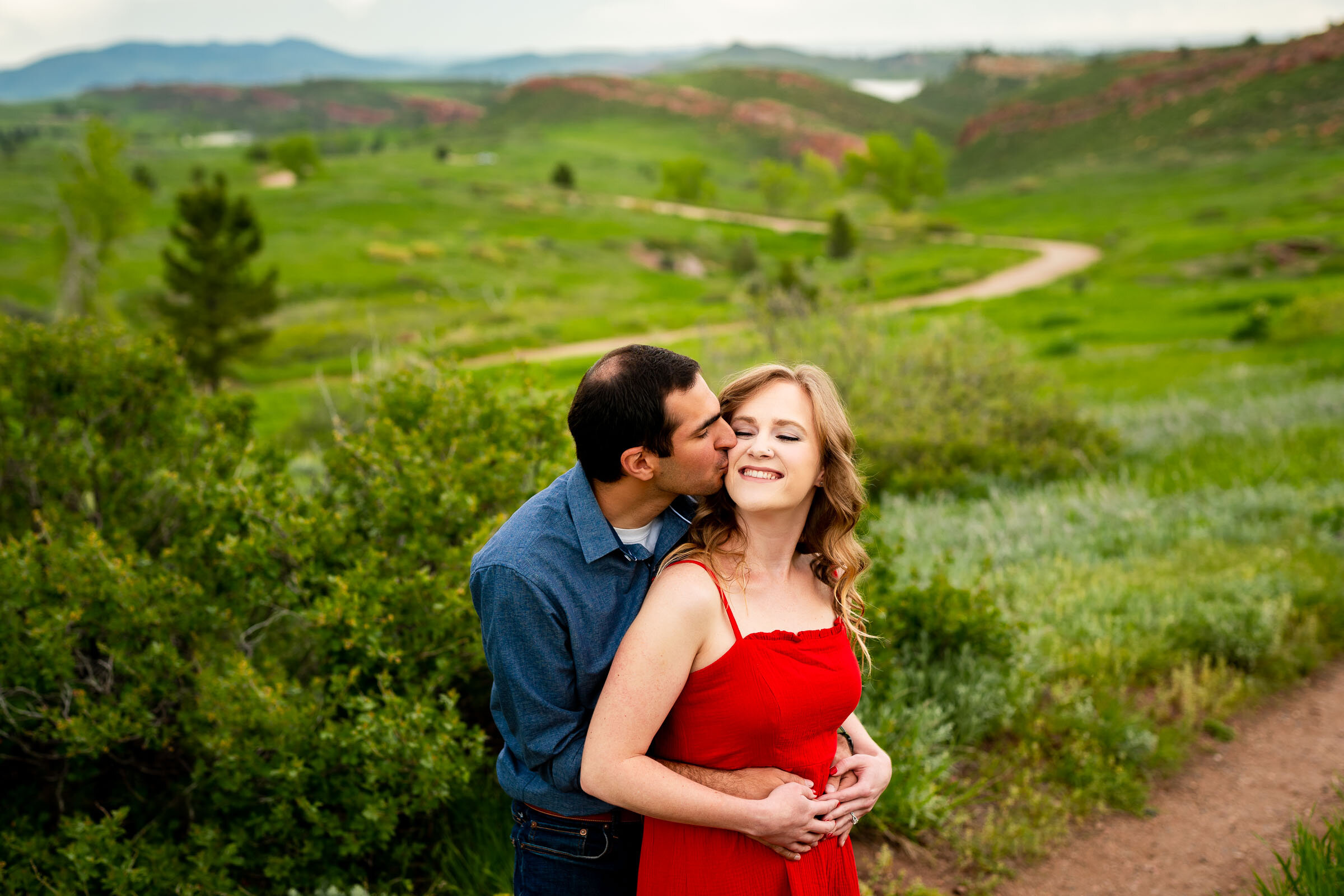 Engaged couple embraces in a luscious green landscape of rolling foothills during golden hour, Engagement Photos, Engagement Photo Inspiration, Engagement Photography, Engagement Photographer, Spring Engagement Photos, Fort Collins Engagement Photos, Fort Collins engagement photos, Fort Collins engagement photography, Fort Collins engagement photographer, Colorado engagement photos, Colorado engagement photography, Colorado engagement inspiration, Horsetooth Reservoir Engagement
