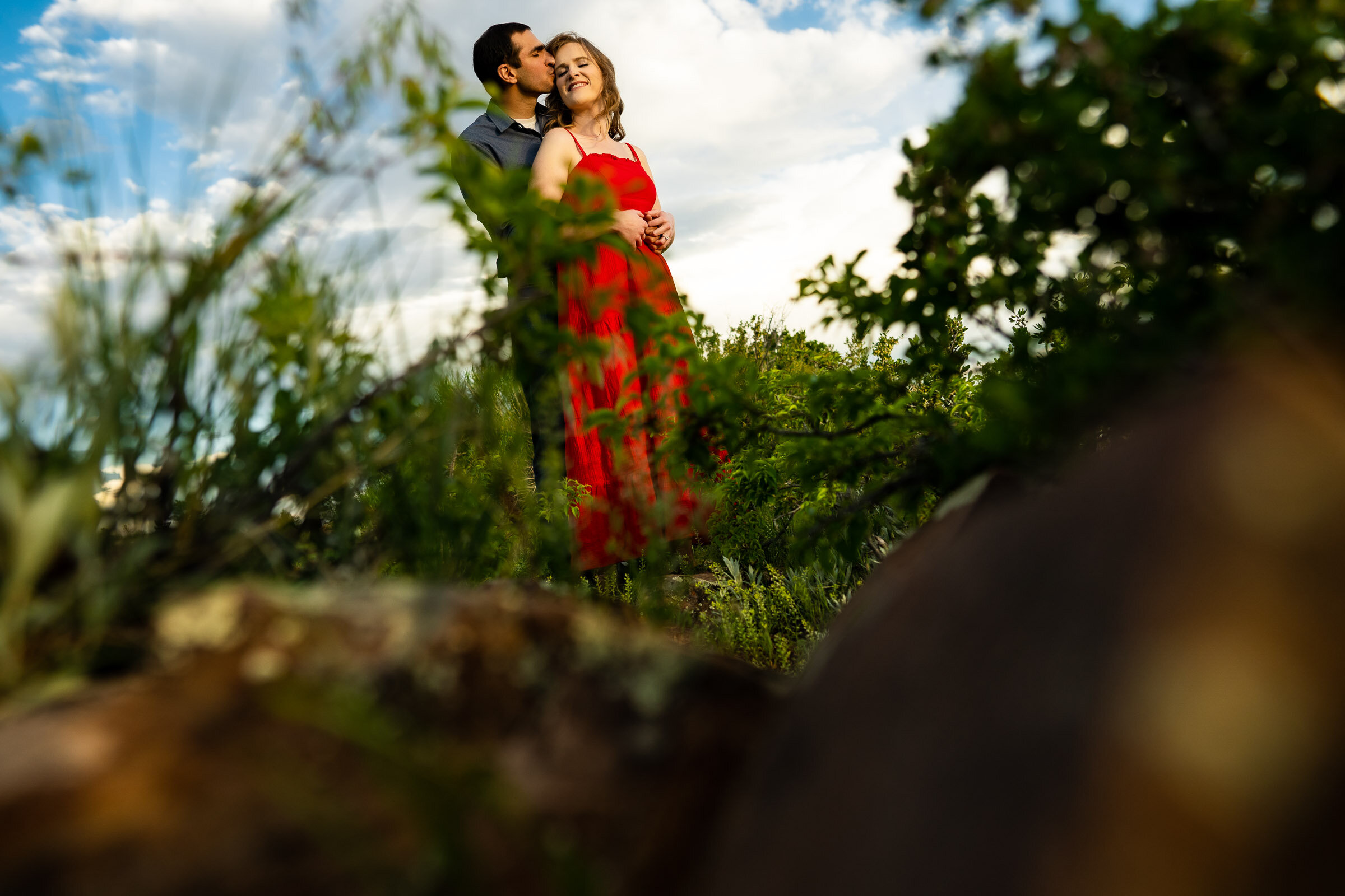 Engaged couple embraces in a luscious green landscape in the foothills during golden hour by the water, Engagement Photos, Engagement Photo Inspiration, Engagement Photography, Engagement Photographer, Spring Engagement Photos, Fort Collins Engagement Photos, Fort Collins engagement photos, Fort Collins engagement photography, Fort Collins engagement photographer, Colorado engagement photos, Colorado engagement photography, Colorado engagement inspiration, Horsetooth Reservoir Engagement