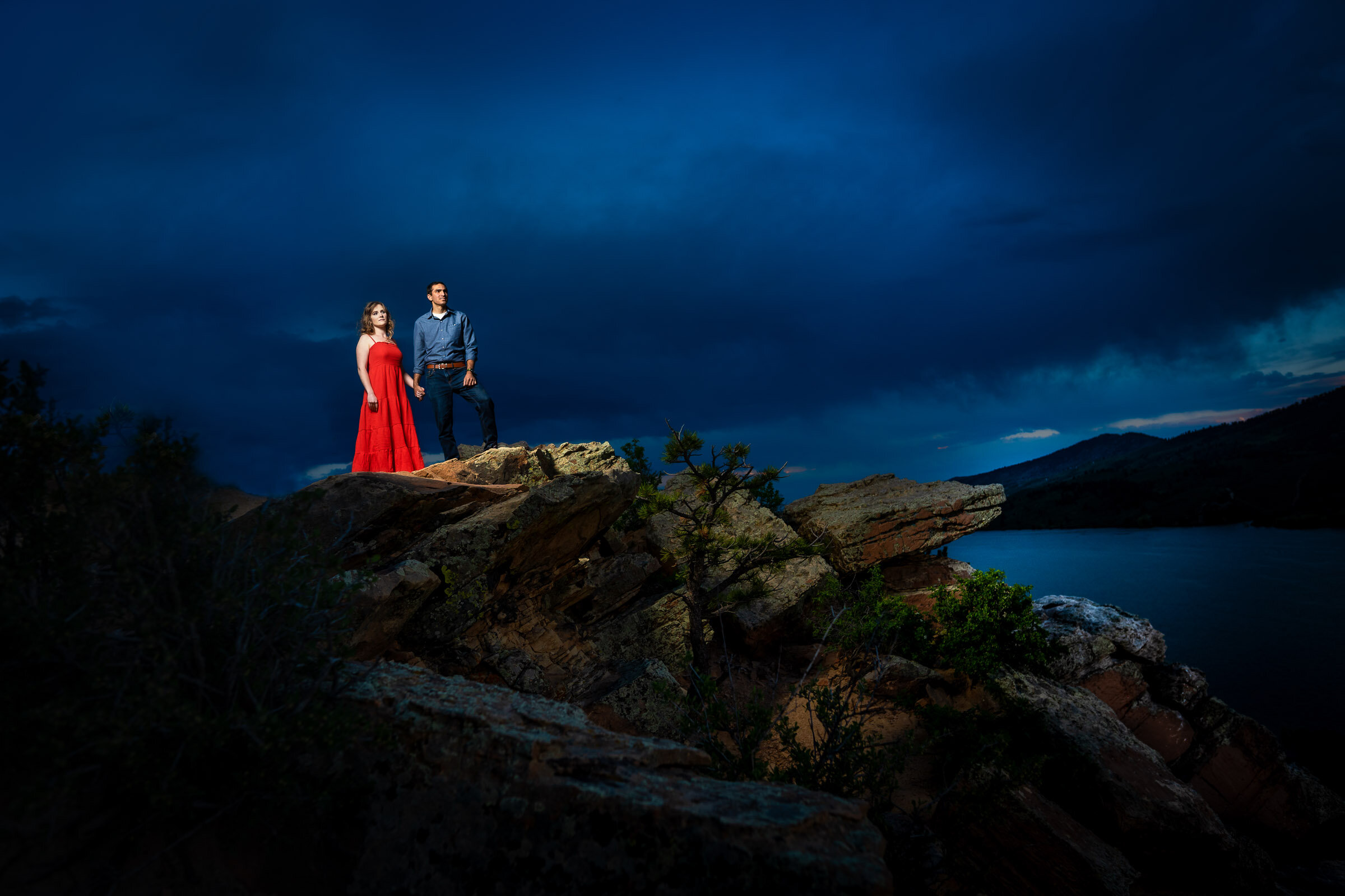 Engaged couple hold hands as they stand atop a rocky ledge overlooking the water during blue hour, Engagement Photos, Engagement Photo Inspiration, Engagement Photography, Engagement Photographer, Spring Engagement Photos, Fort Collins Engagement Photos, Fort Collins engagement photos, Fort Collins engagement photography, Fort Collins engagement photographer, Colorado engagement photos, Colorado engagement photography, Colorado engagement inspiration, Horsetooth Reservoir Engagement