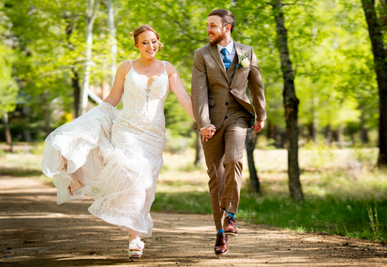 Bride and groom skip down a dirt road that runs through an aspen grove in Estes Park