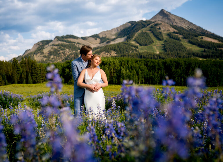 Newlyweds embrace in a field full of lupin wildflowers at the base of Mount Crested Butte during golden hour at Ten Peaks at Crested Butte Mountain Resort on their wedding day