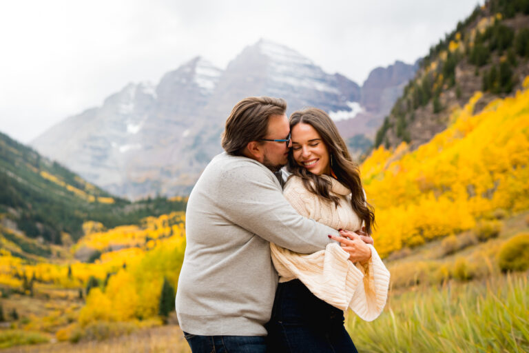 Couple hugs with yellow aspens and glowing fall color and Maroon Peak behind them