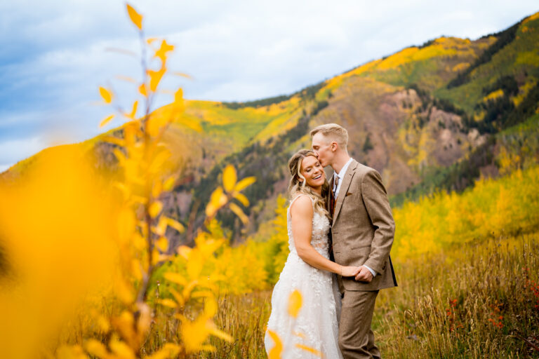 Bride and groom kiss among the yellow aspens with the mountain behind them during their wedding at T Lazy 7 Ranch in Aspen Colorado