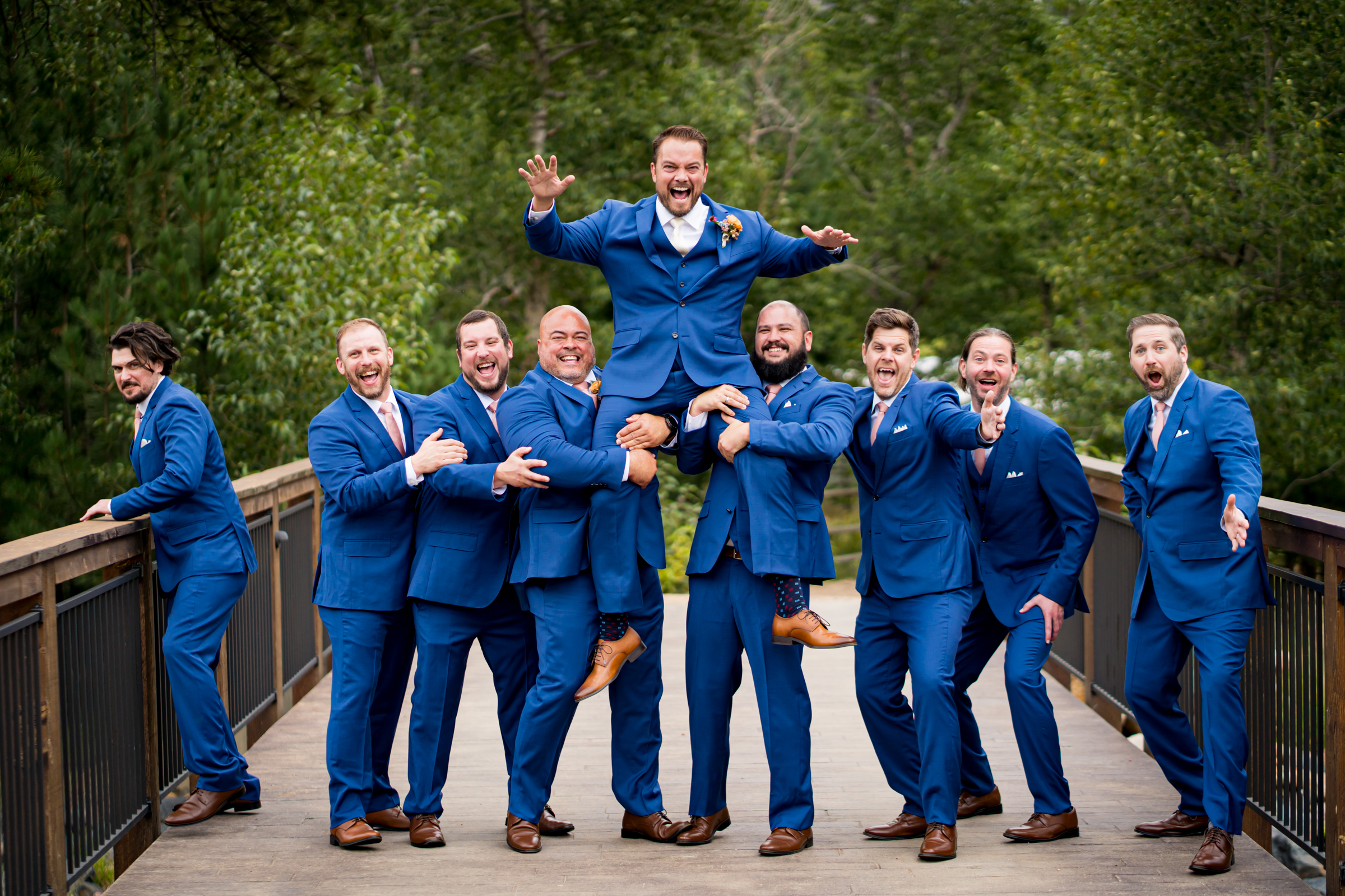 Groomsmen lift the groom on a bridge for wedding party photos