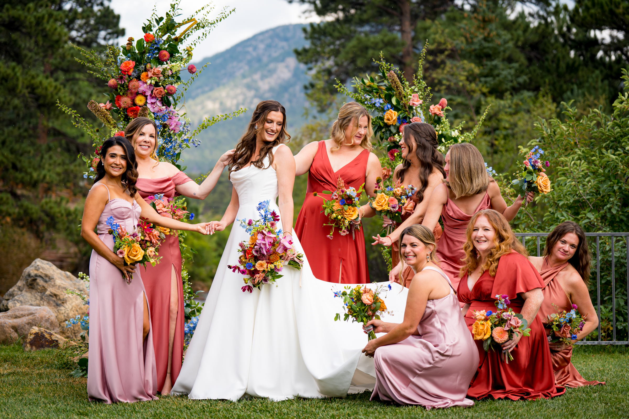 Bridesmaids pamper the bride in front of the flower arch with the mountains and river in the distance as the backdrop