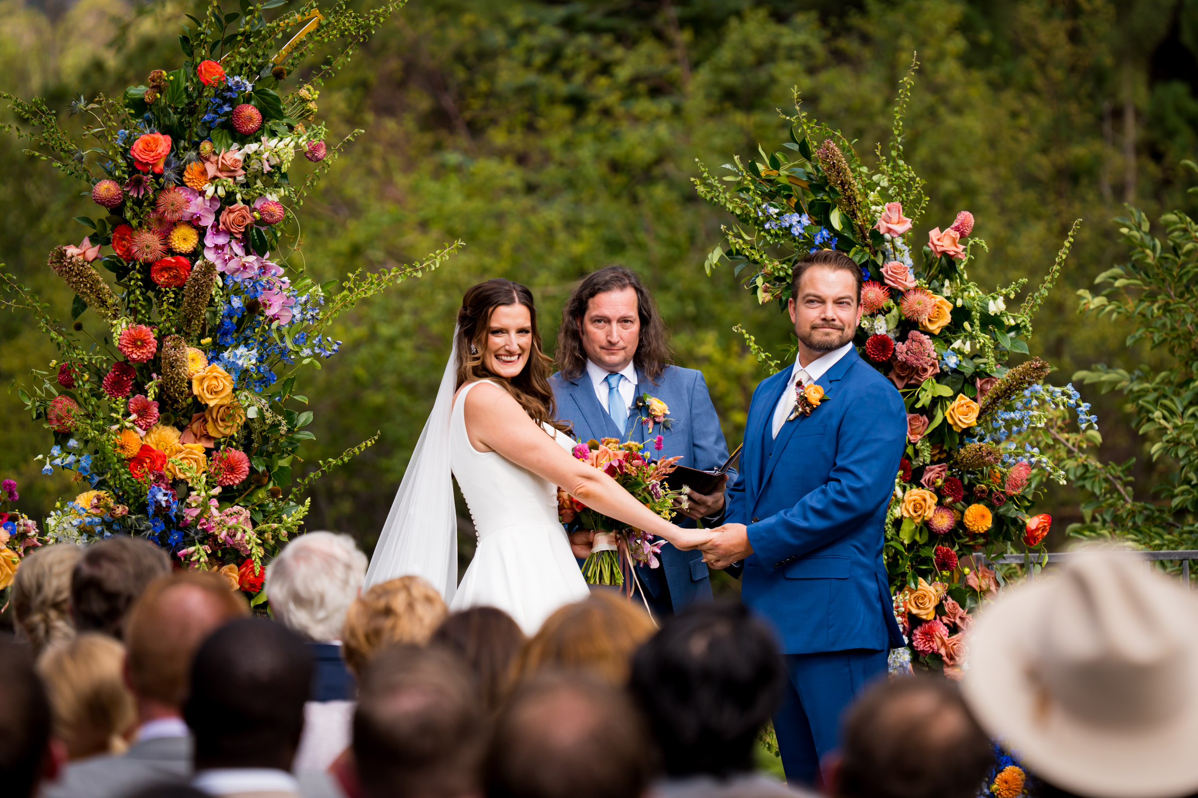 Bride and groom stand at the altar decorated in colorful summer flowers during there wedding ceremony, with the mountains and river as the backdrop
