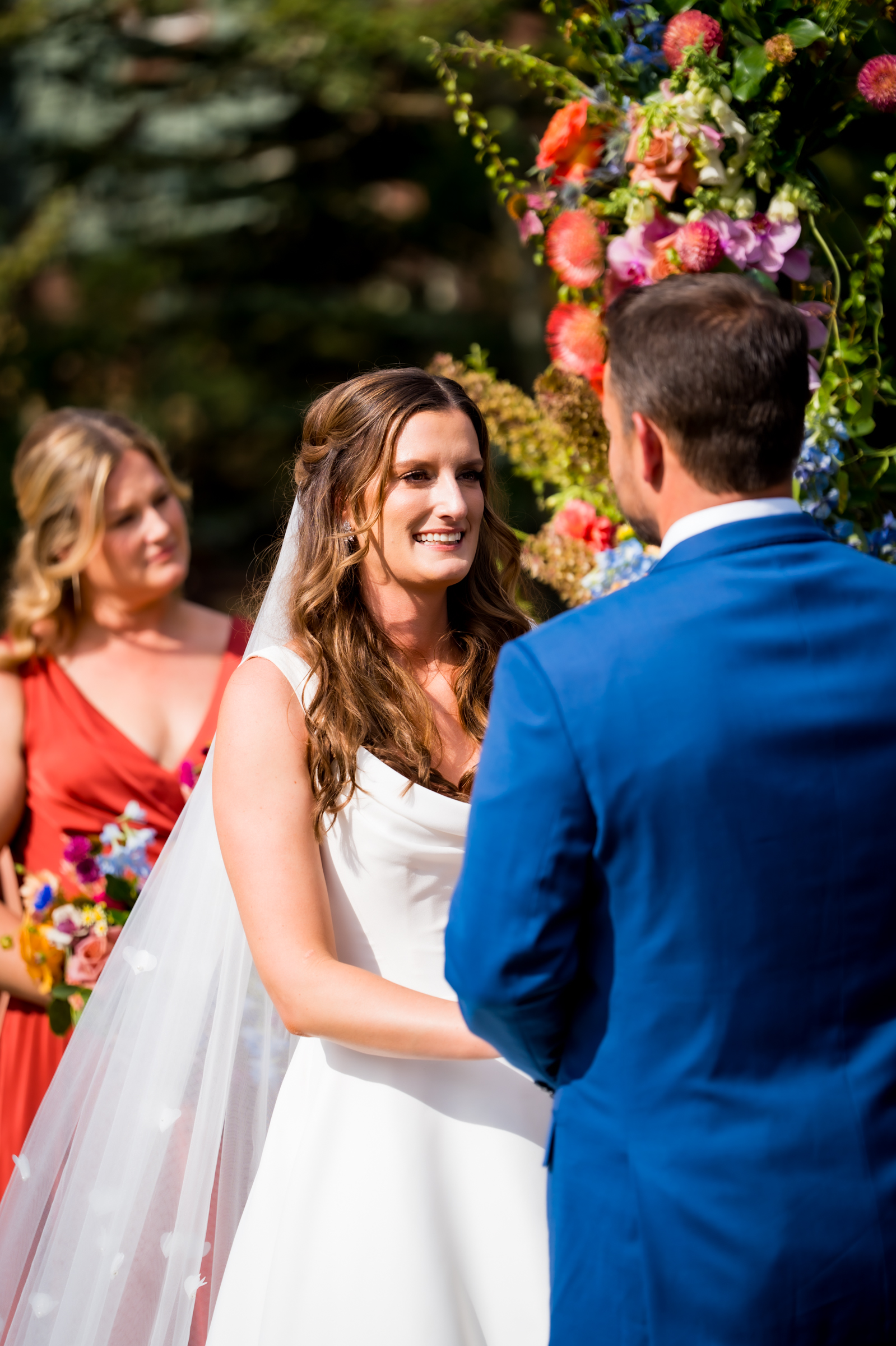 Bride and groom stand at the altar decorated in colorful summer flowers during there wedding ceremony, with the mountains and river as the backdrop