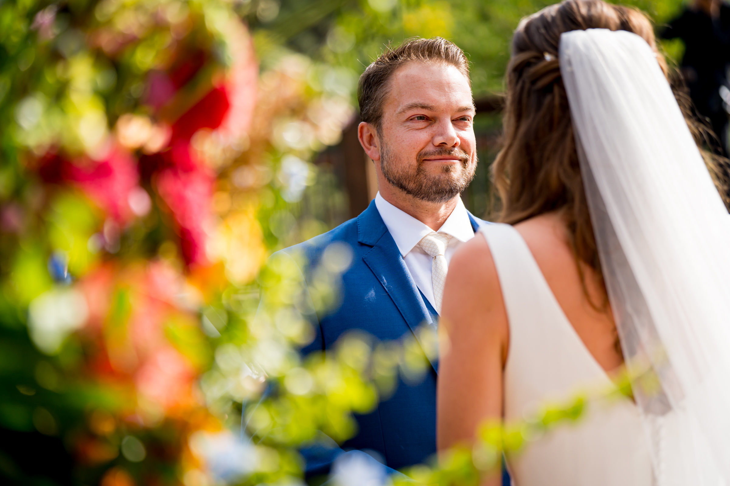 Bride and groom stand at the altar decorated in colorful summer flowers during there wedding ceremony, with the mountains and river as the backdrop
