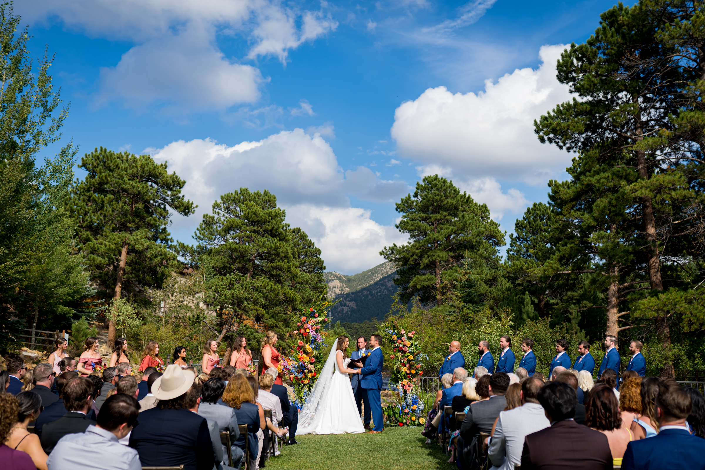 Bride and groom stand at the altar decorated in colorful summer flowers during there wedding ceremony, with the mountains and river as the backdrop