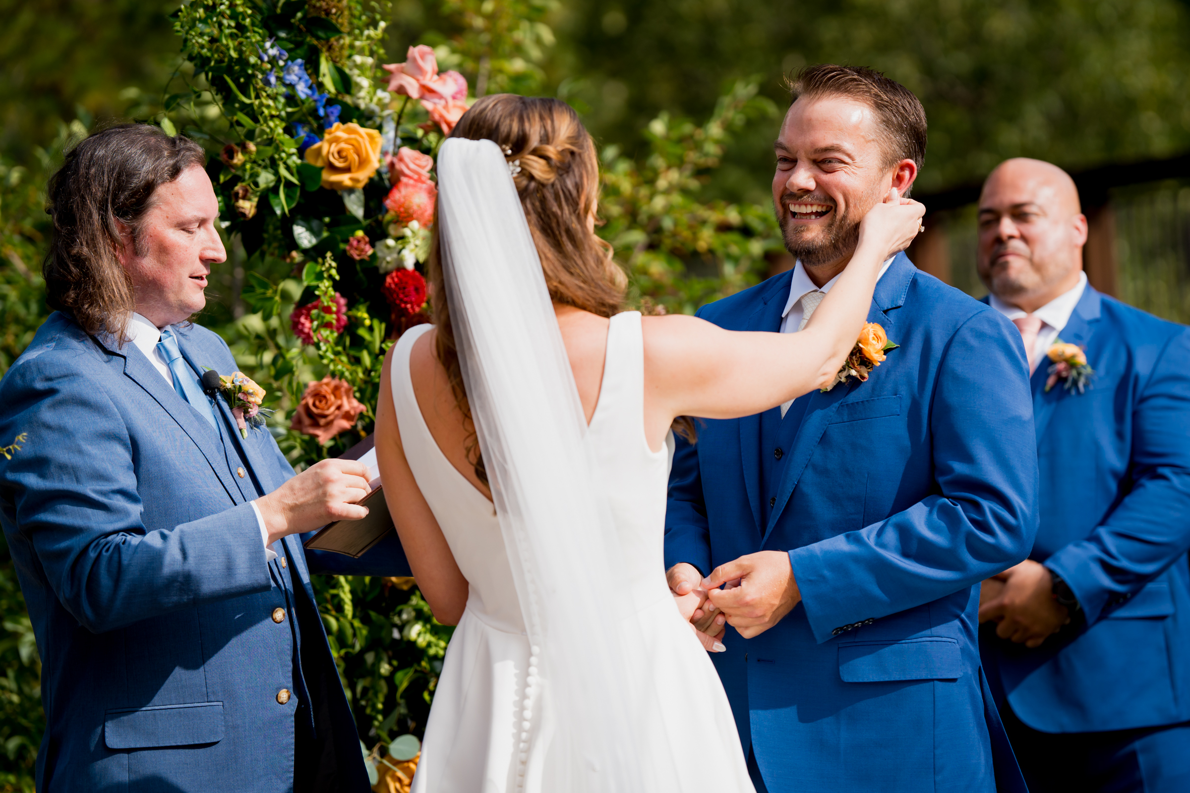 Bride and groom stand at the altar decorated in colorful summer flowers during there wedding ceremony, with the mountains and river as the backdrop