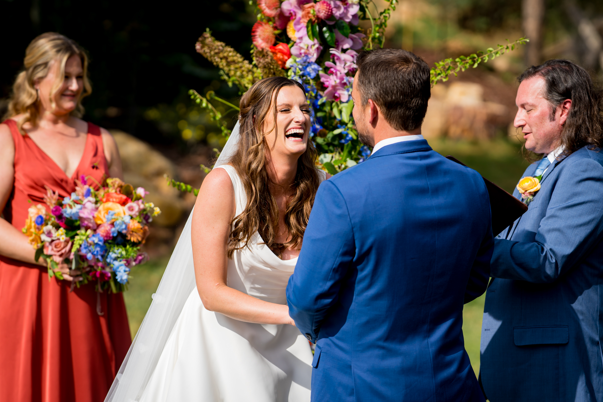 Bride and groom stand at the altar decorated in colorful summer flowers during there wedding ceremony, with the mountains and river as the backdrop